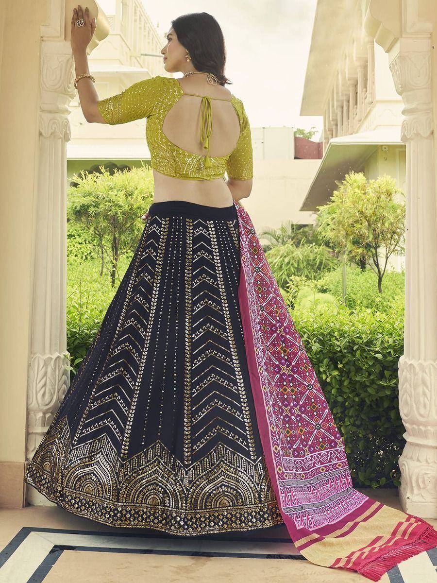 Woman in green embroidered blouse and black lehenga with gold patterns, paired with pink dupatta, showcasing Indian ethnic wear.