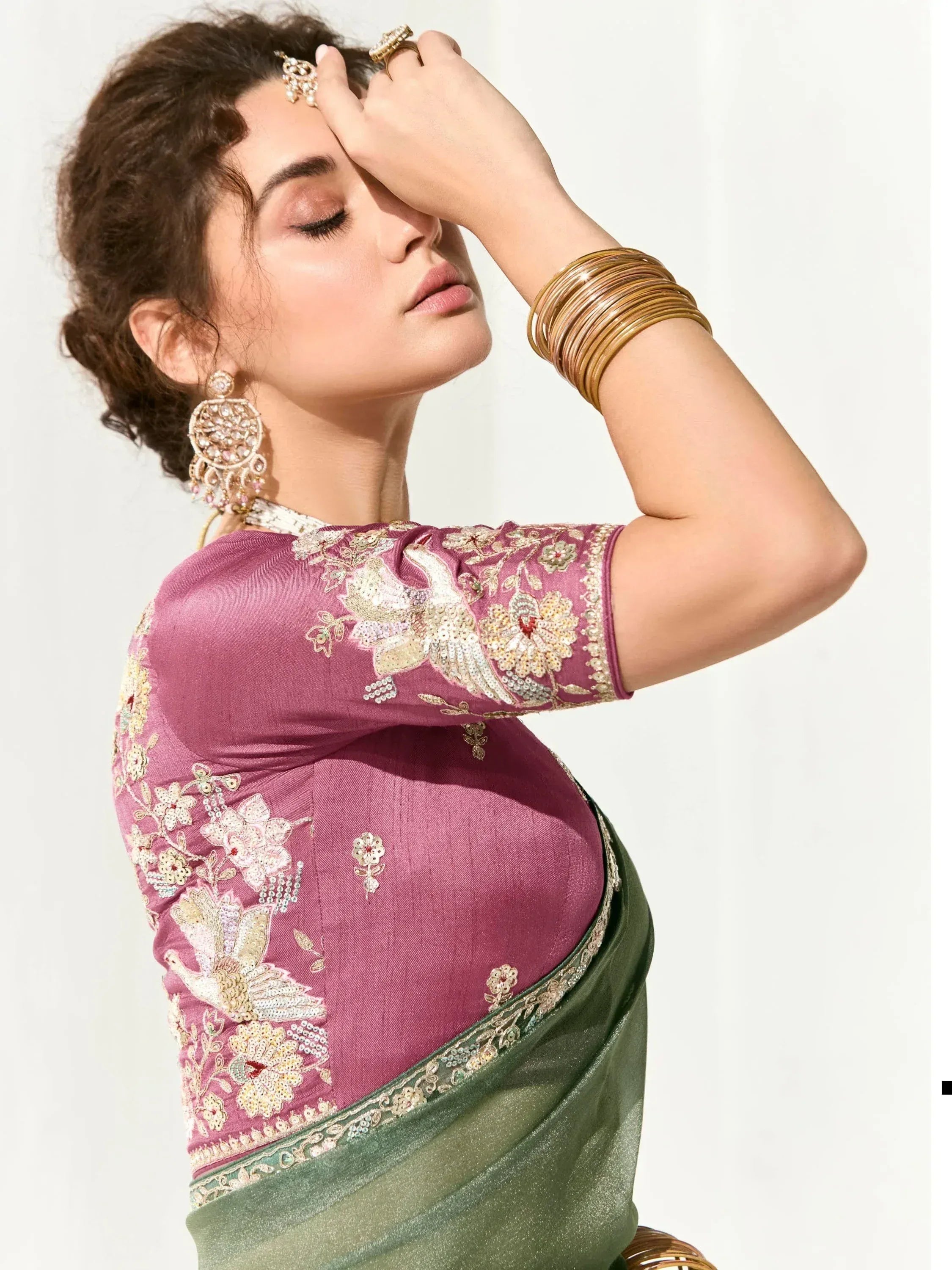 Woman in pink embroidered blouse with green saree, gold jewelry, and floral bird motifs for Indian ethnic wear.