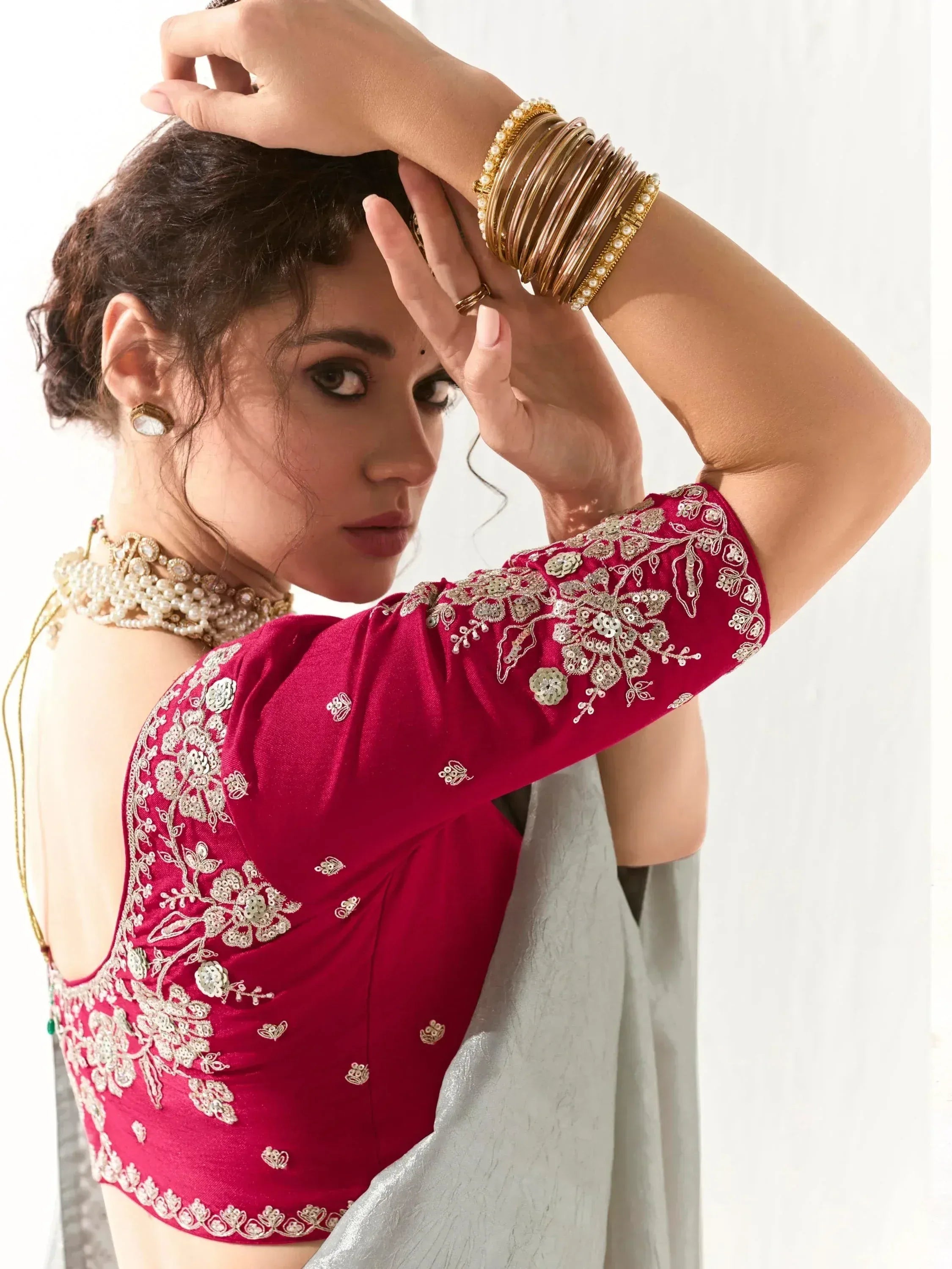 Red embroidered blouse with gold detailing, paired with grey saree and traditional jewelry for ethnic wear