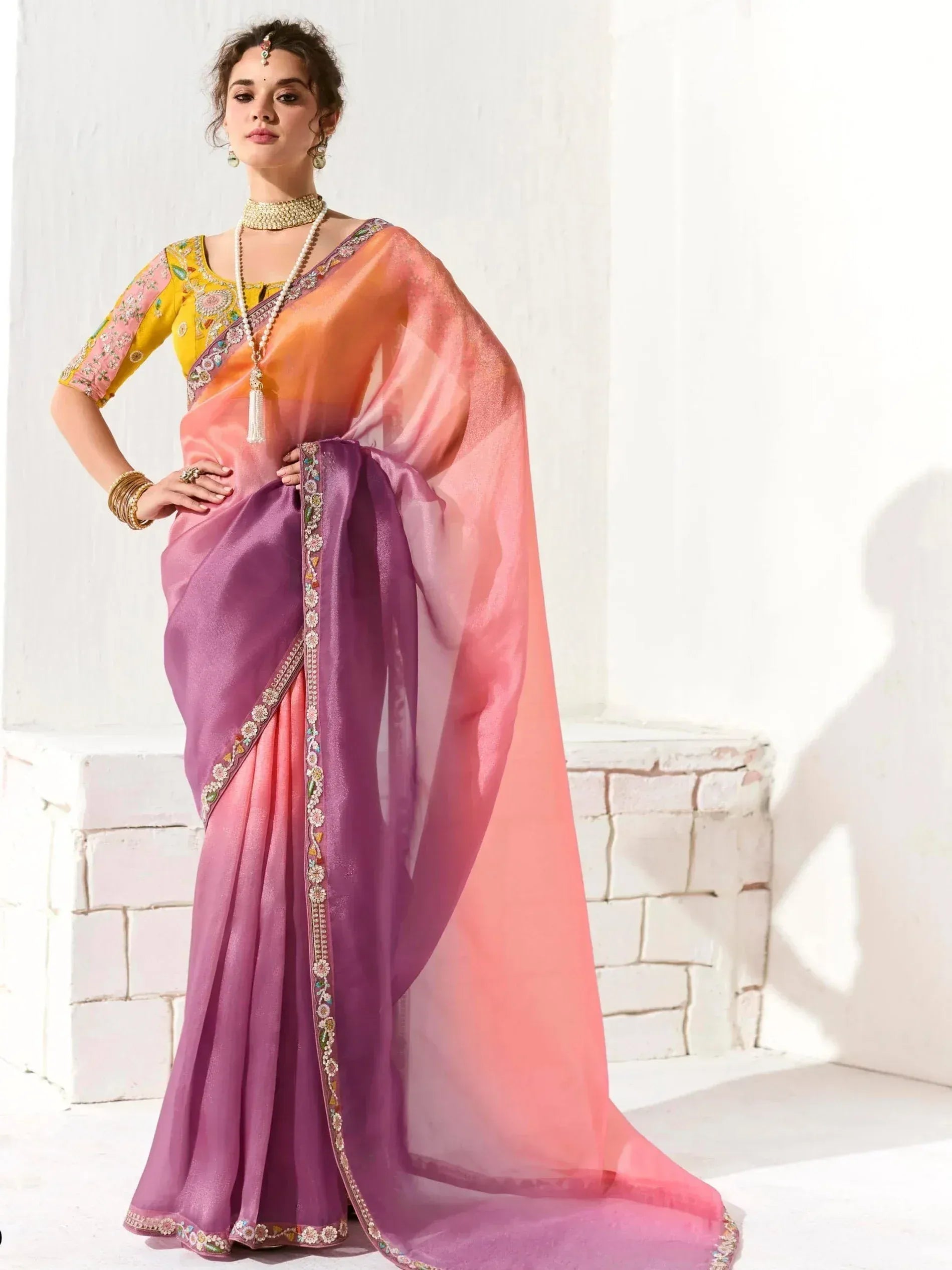 Woman in vibrant purple and pink ombre saree with floral embroidery, paired with yellow blouse and traditional jewelry.