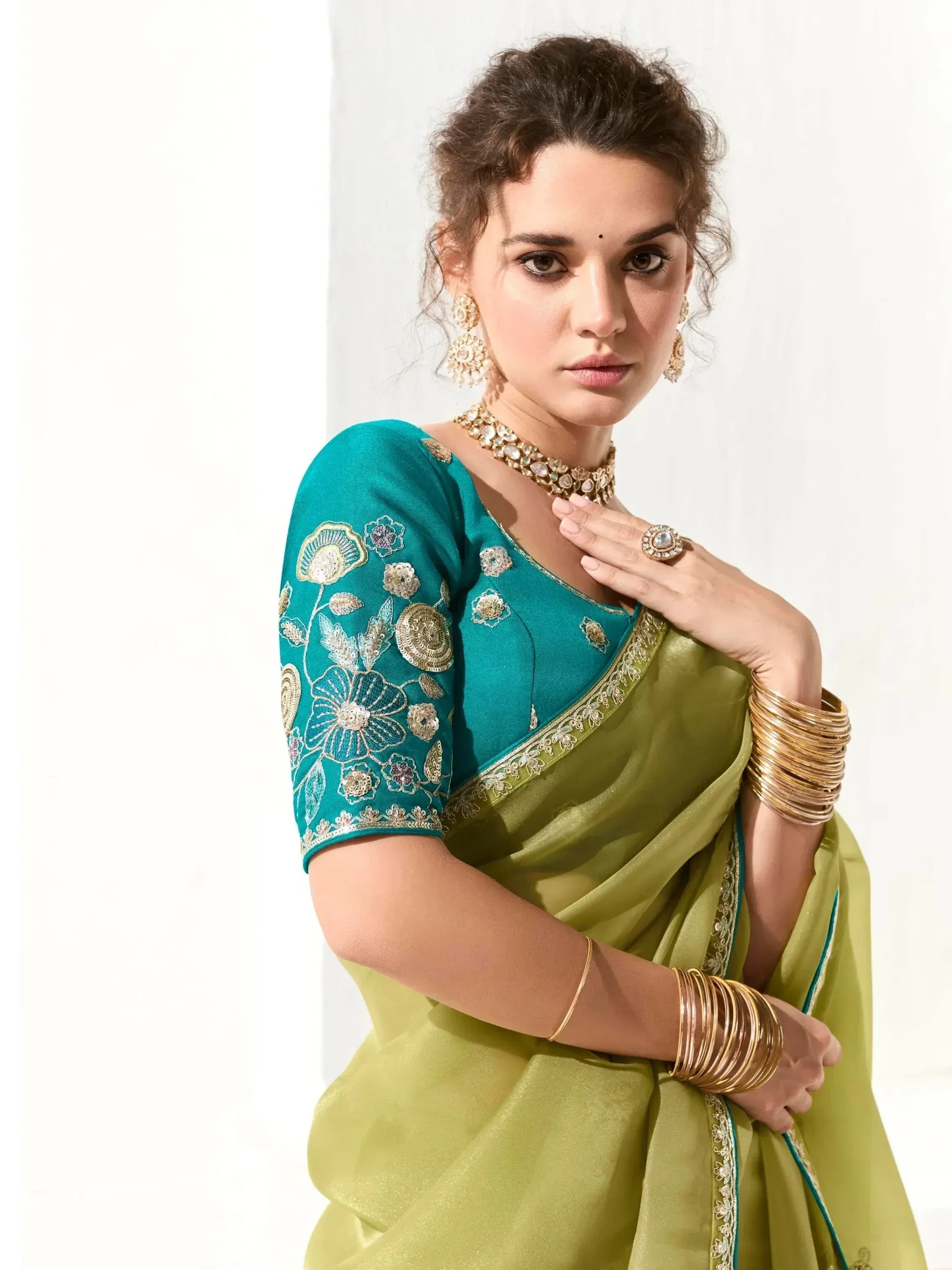 Woman in green saree with floral embroidered blouse, gold jewelry, and traditional Indian ethnic wear