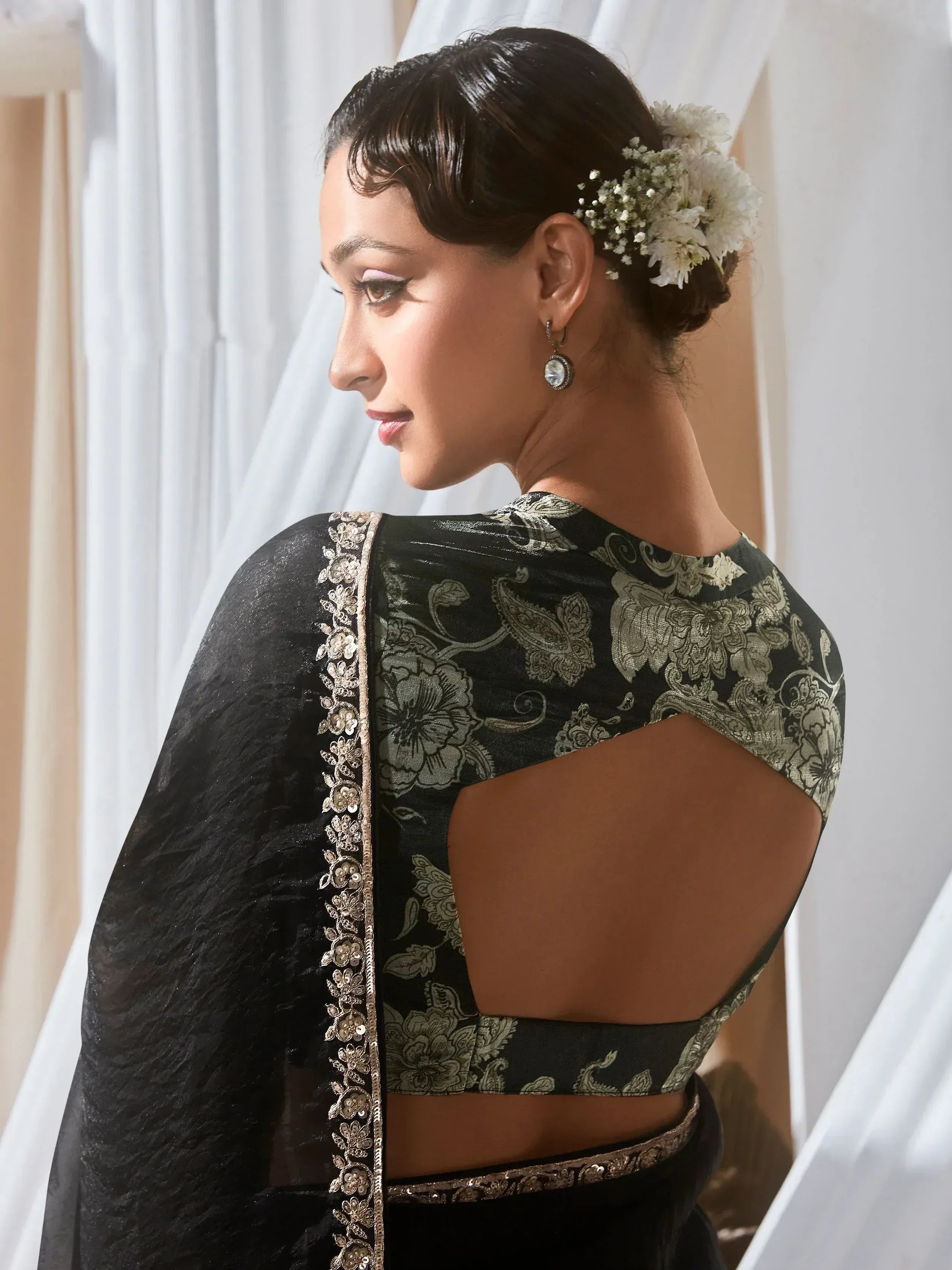 Black floral embroidered saree blouse with cut-out back, gold detailing, and white floral hair accessory