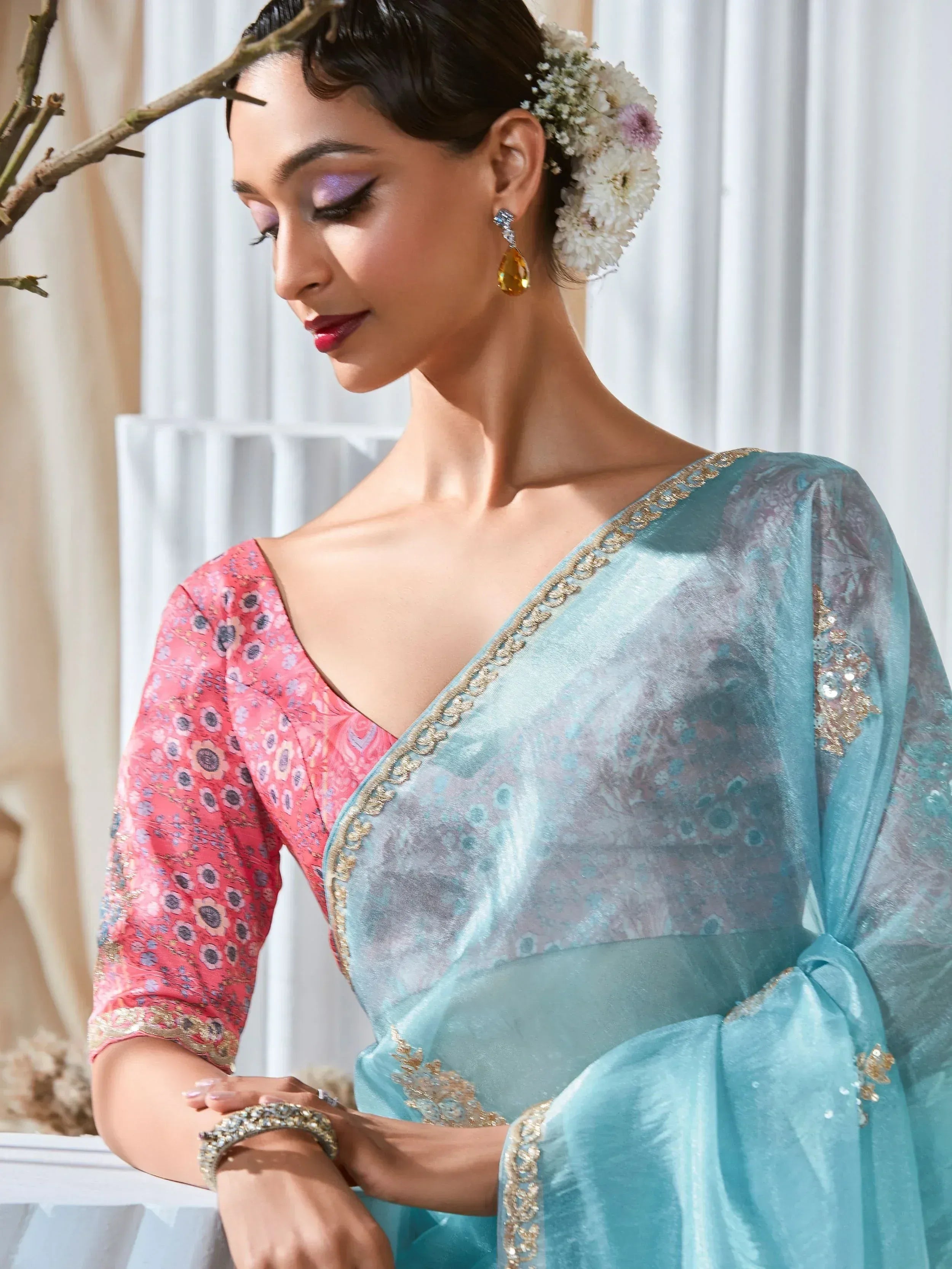 Elegant woman in turquoise saree with floral pink blouse, gold embroidery, and floral hair accessory