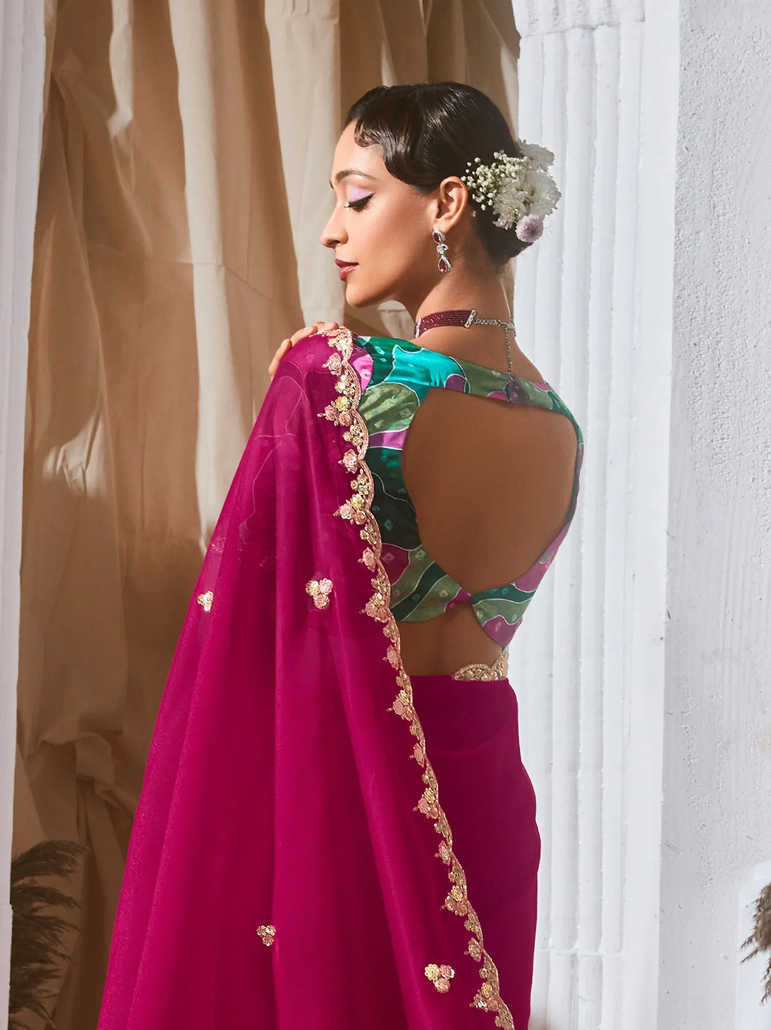 Woman in vibrant pink saree with floral embroidery and open-back blouse, styled with floral hair accessory