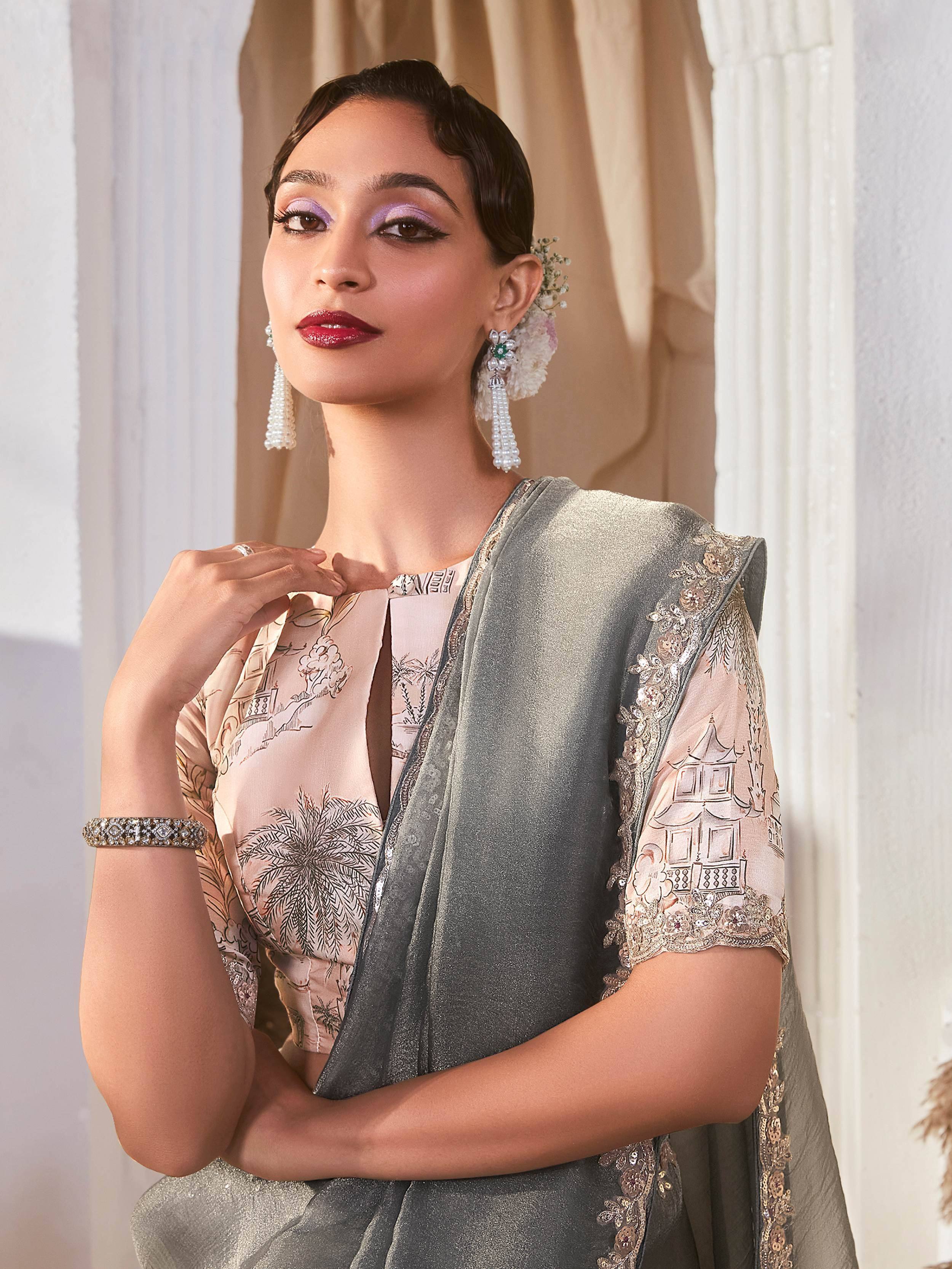 Elegant woman in designer Indian ethnic wear with printed blouse and embroidered grey dupatta, styled with pearl earrings.