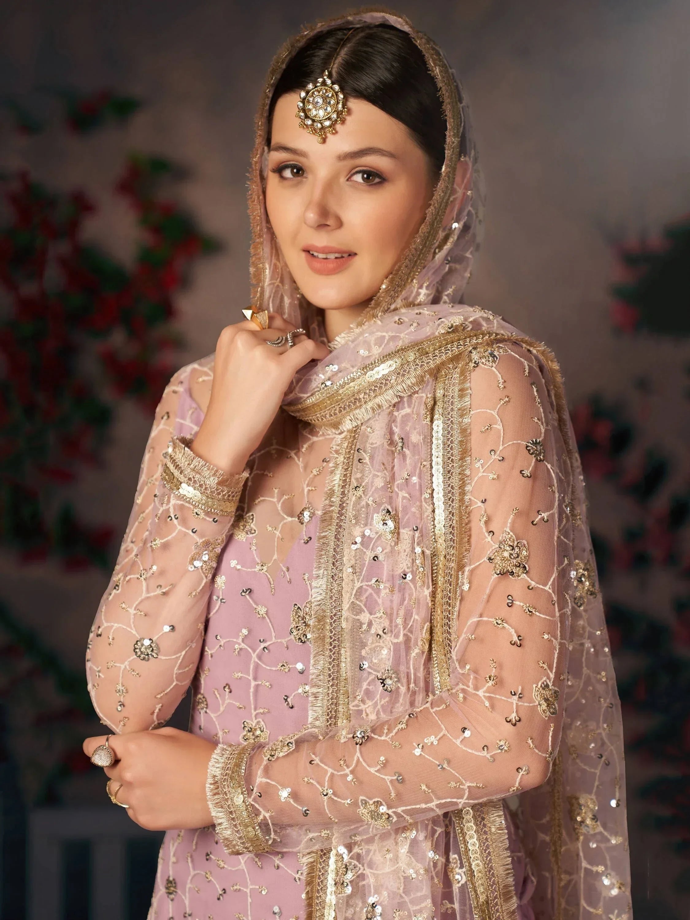 Woman wearing lavender embroidered ethnic gown with gold sequins and traditional jewelry