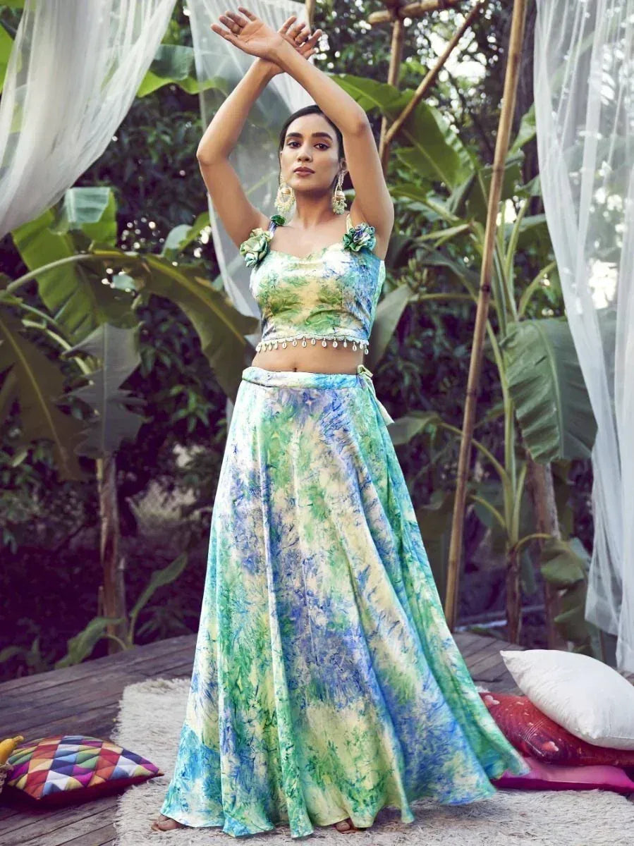 Woman in vibrant tie-dye lehenga choli with floral top, posing outdoors under sheer drapes
