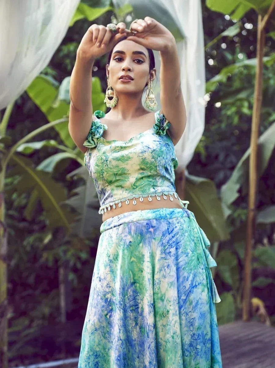 Woman in green and blue printed lehenga choli with floral top and embellished waist, styled with statement earrings