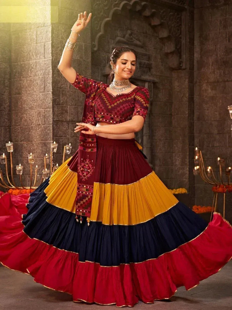 Woman dancing in vibrant maroon, yellow, and navy lehenga choli with embroidered blouse and dupatta