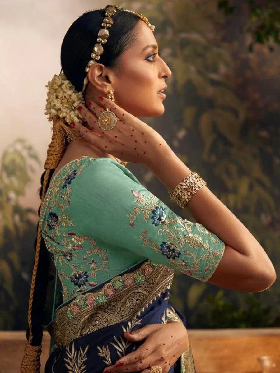 Elegant woman in turquoise embroidered saree with gold jewelry and floral hair accessory