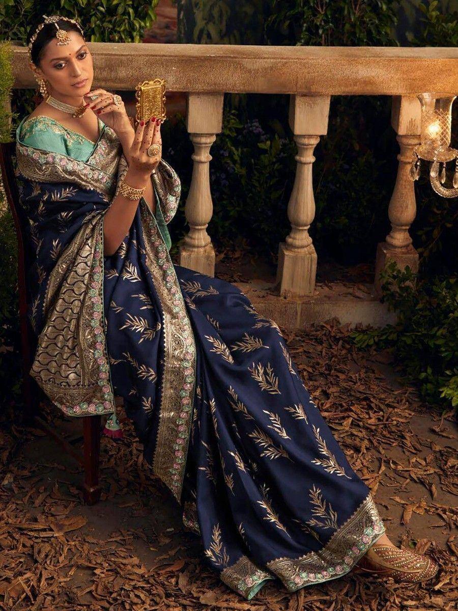 Woman in navy blue designer saree with gold leaf print and embroidered border, paired with green blouse and traditional jewelry.