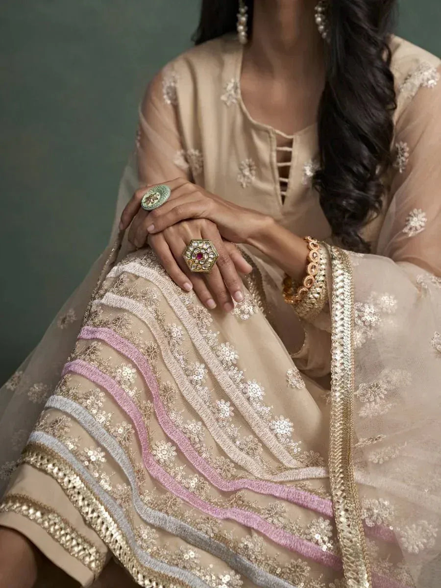 Beige embroidered salwar kameez with pink and gold detailing, paired with statement rings and earrings.