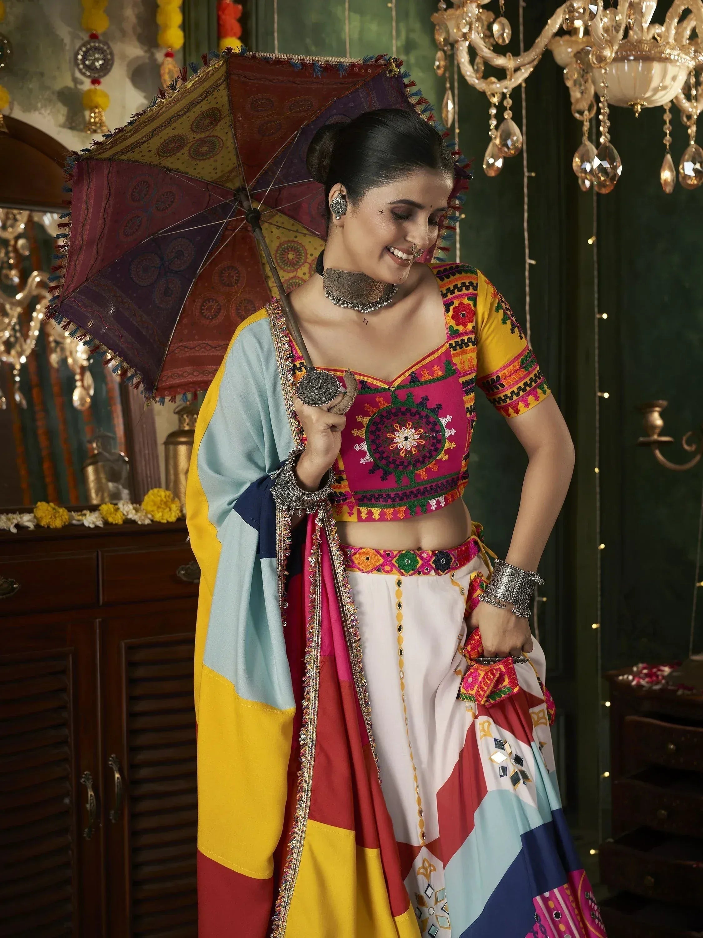 Woman in colorful embroidered lehenga choli with mirror work, holding patterned umbrella, traditional Indian ethnic wear