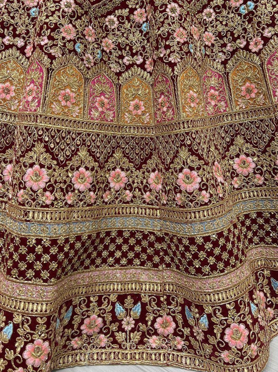 Maroon velvet lehenga with gold and pink floral embroidery, perfect for Indian weddings and festive occasions.
