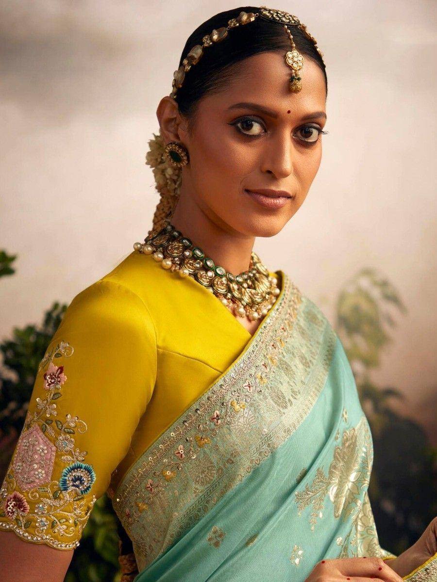 Elegant woman in turquoise saree with gold embroidery, yellow blouse, and traditional Indian jewelry