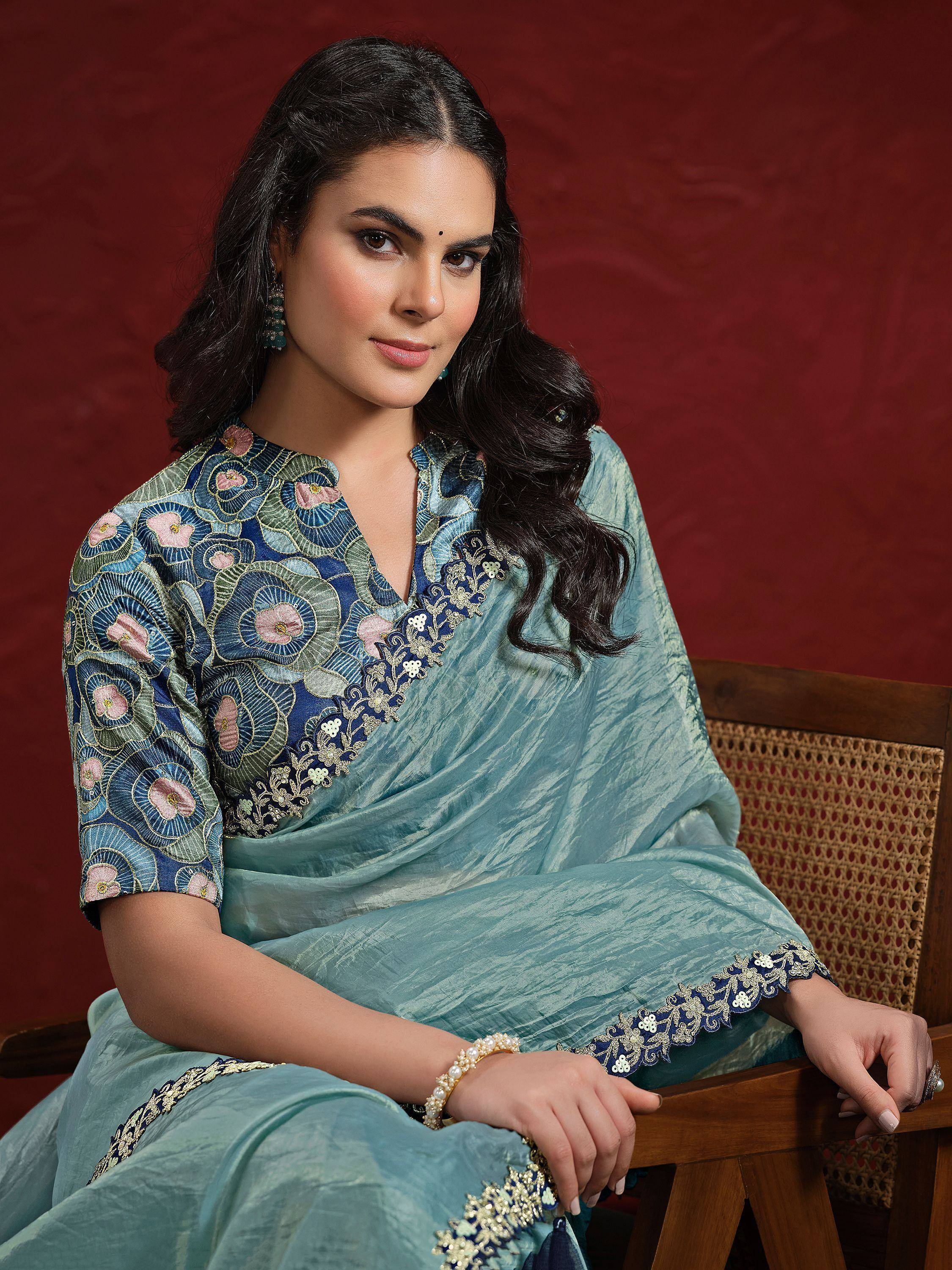 Woman in blue floral embroidered ethnic gown with gold detailing, seated on wooden chair