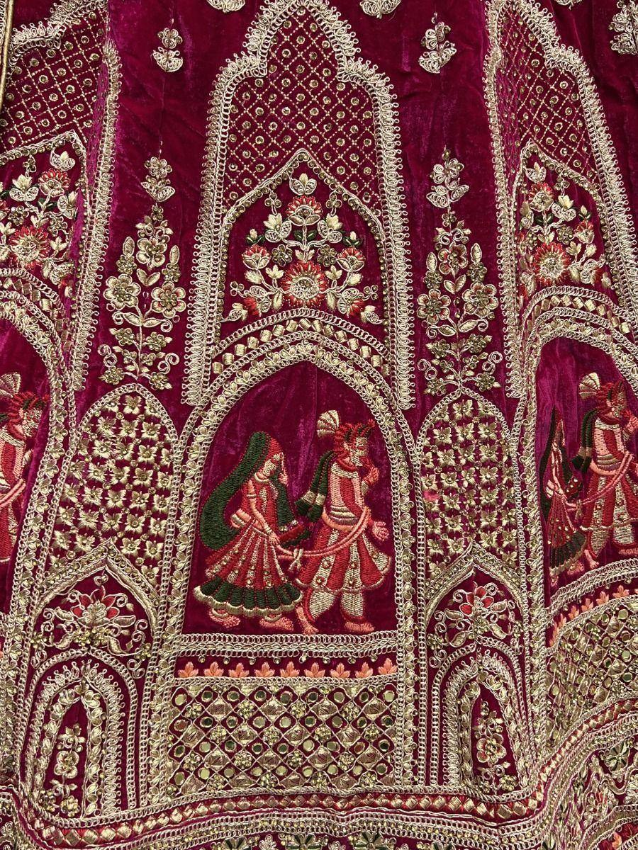 Richly embroidered maroon velvet lehenga with gold floral motifs and traditional couple scenes