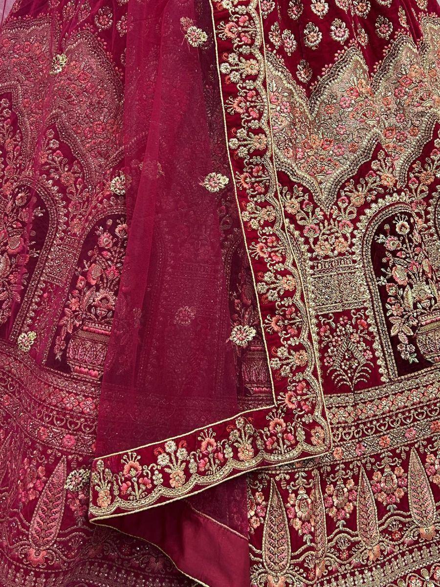 Rich maroon velvet lehenga choli with intricate gold and pink floral embroidery, perfect for weddings.