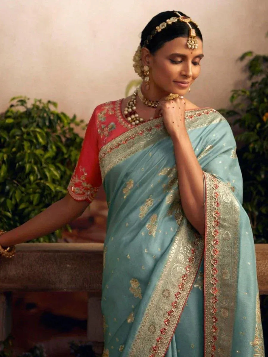 Elegant woman in light blue saree with gold embroidery and red blouse, styled with traditional Indian jewelry