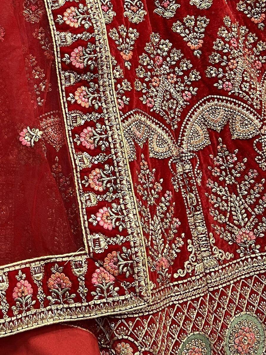 Red velvet lehenga choli with intricate gold and pink floral embroidery, perfect for Indian weddings.