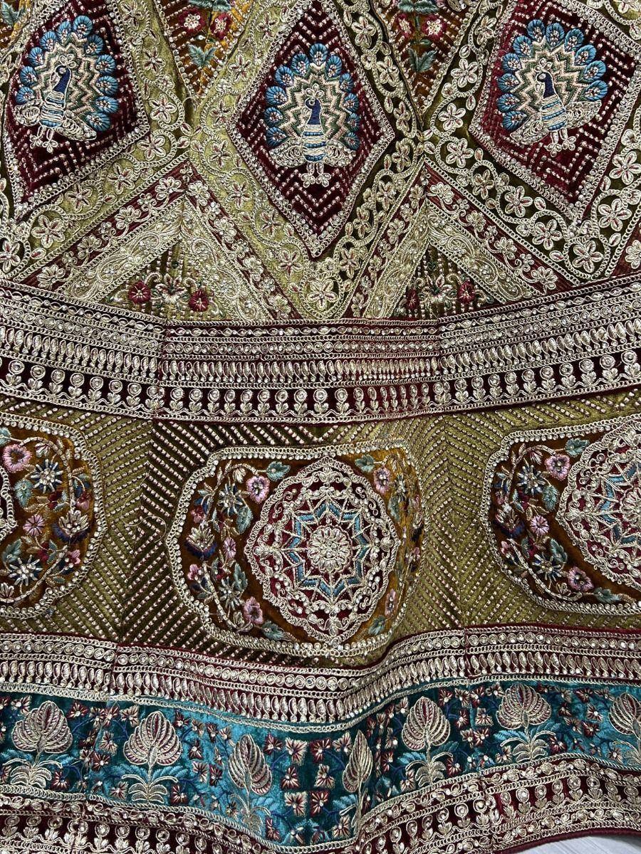 Richly embroidered Indian lehenga with peacock motifs, floral patterns, and intricate zari work in maroon, gold, and teal.