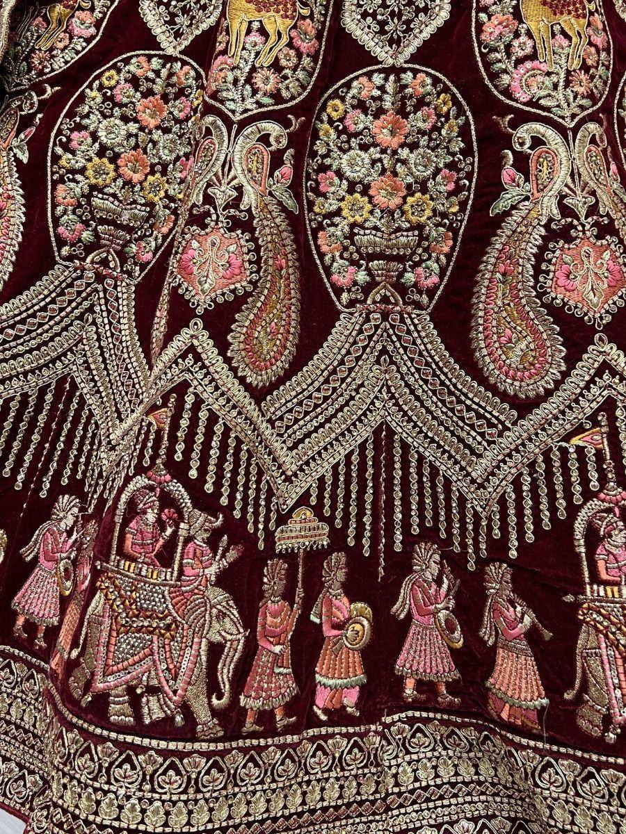 Richly embroidered maroon lehenga with floral motifs, peacocks, and royal procession detailing for Indian ethnic wear.
