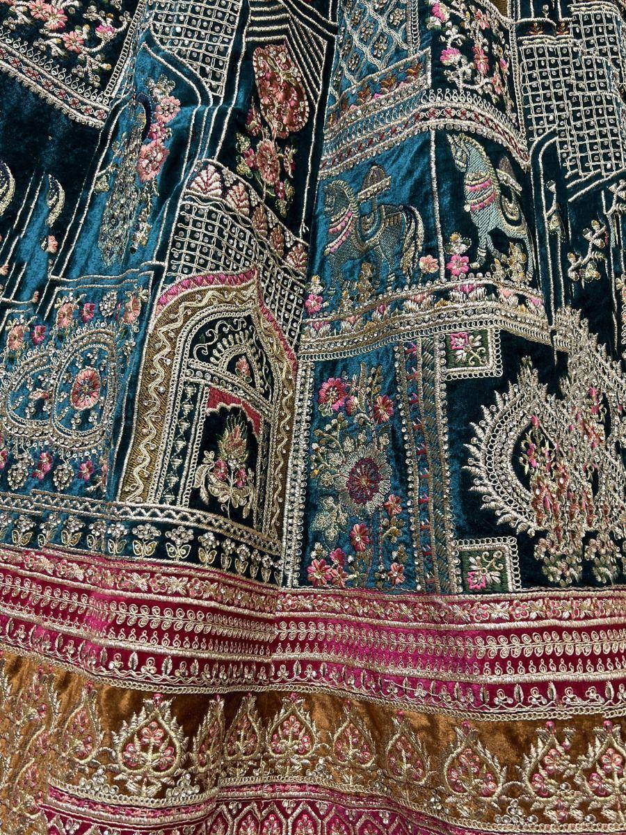 Richly embroidered Indian lehenga with floral and elephant motifs in teal, pink, and gold velvet.