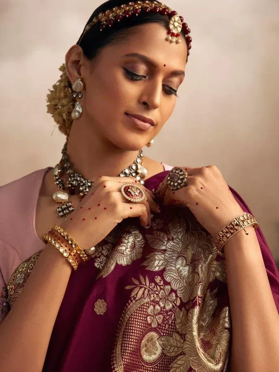 Woman in maroon embroidered saree with gold jewelry and traditional Indian headpiece