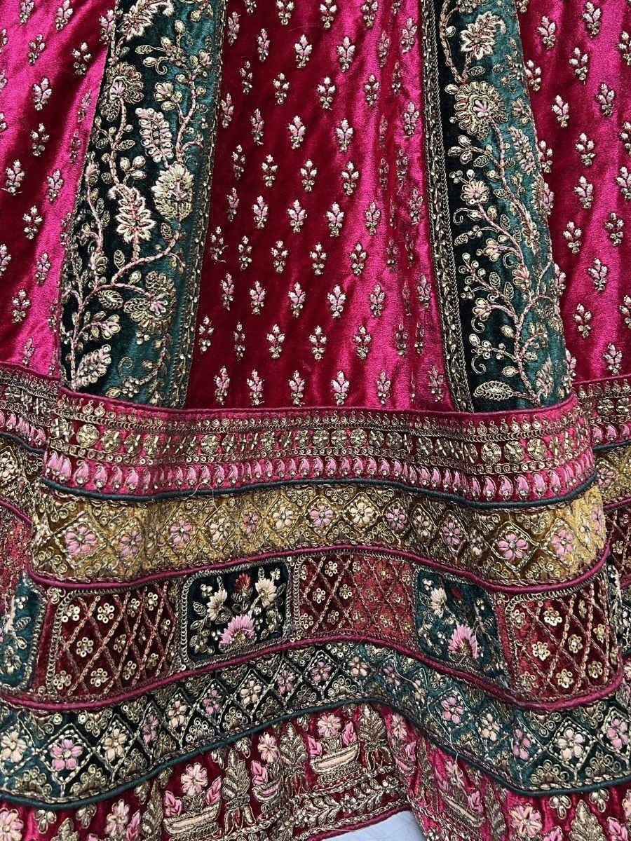 Luxury Indian lehenga with intricate gold embroidery, velvet fabric, and floral motifs in pink and green.