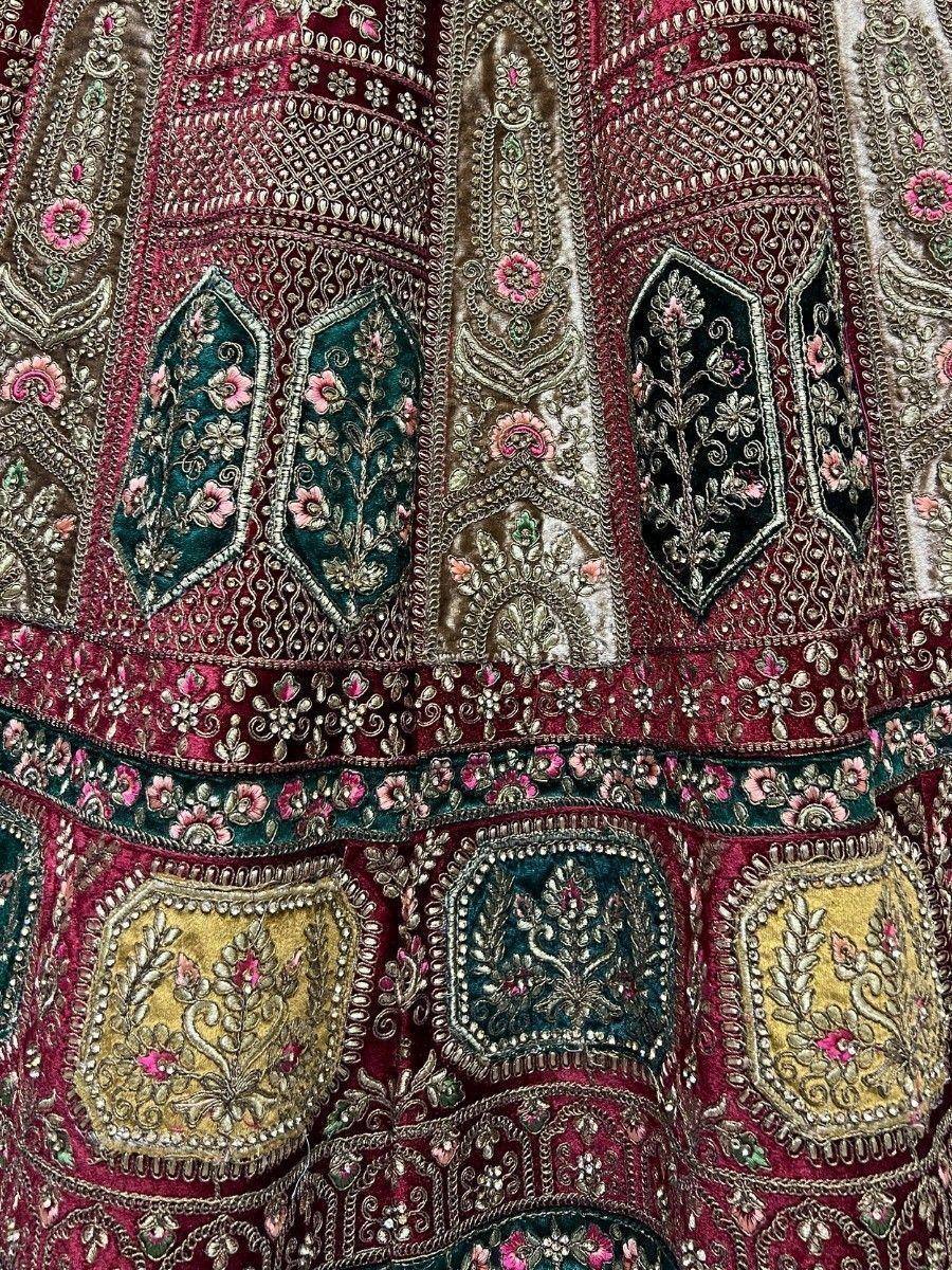 Richly embroidered Indian lehenga with floral motifs, velvet patches, and intricate zari work in maroon, gold, and teal.