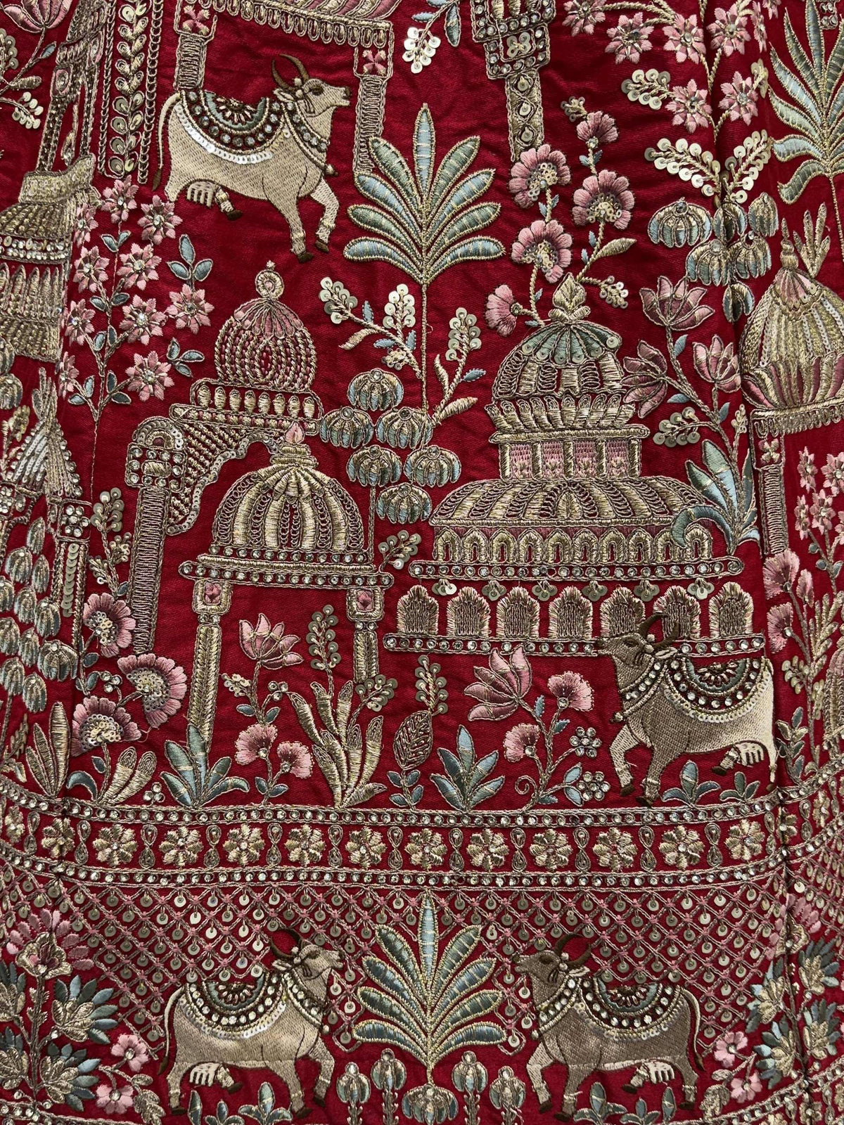 Richly embroidered red ethnic wear with temple motifs, floral designs, and decorative cows for festive occasions.