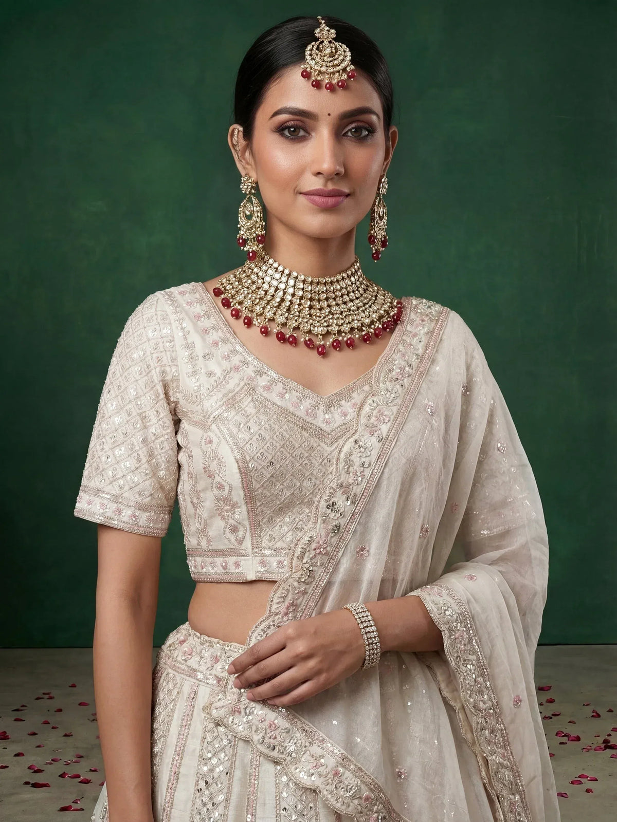 Elegant cream lehenga choli with intricate embroidery and red gemstone jewelry for Indian ethnic wear