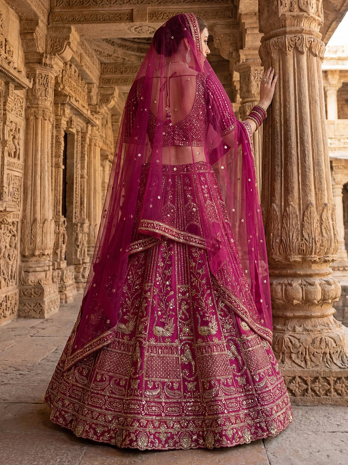 Woman in a heavily embroidered magenta designer lehenga choli with dupatta in a carved temple.