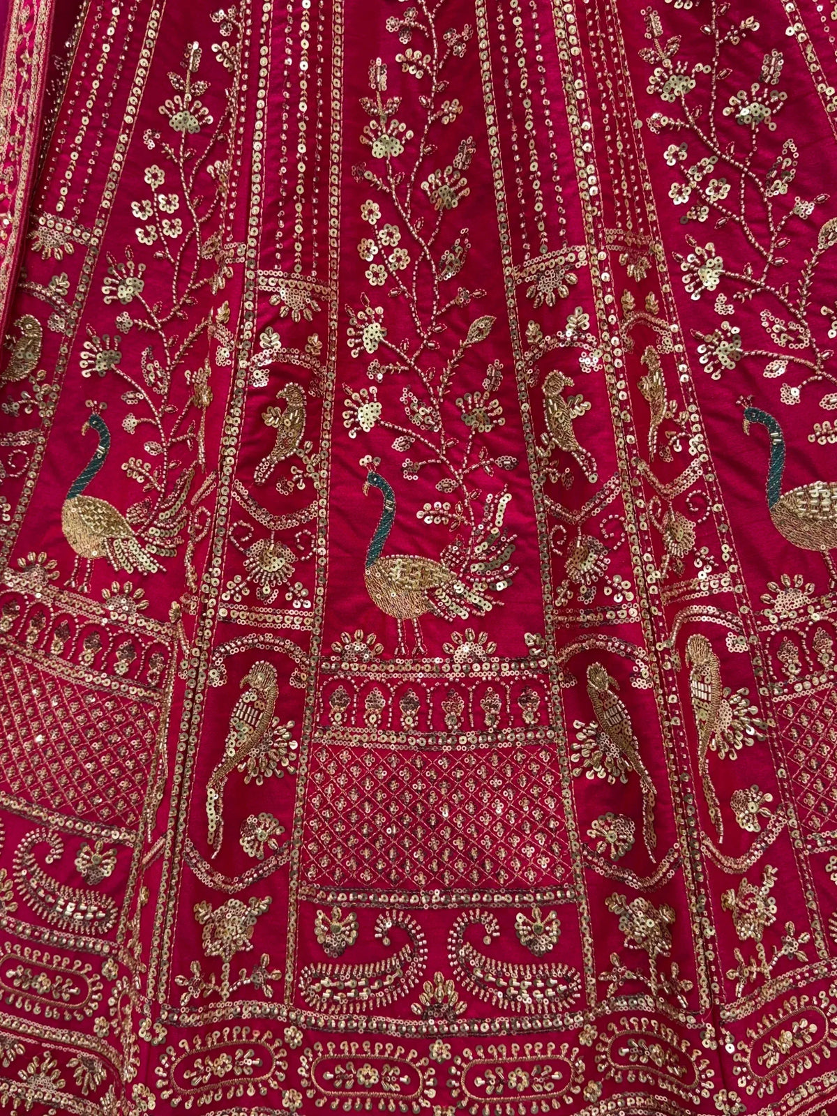Close-up of a magenta designer lehenga with intricate gold zari peacock and floral embroidery.