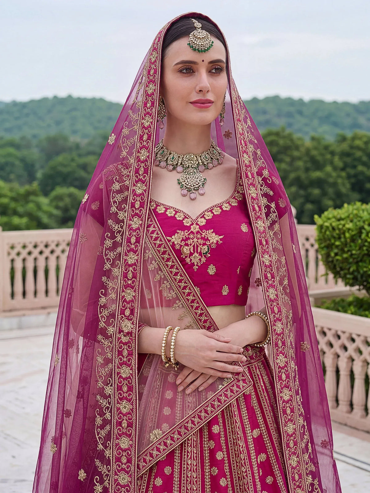Woman wearing a magenta designer lehenga choli with gold embroidery and ethnic jewelry