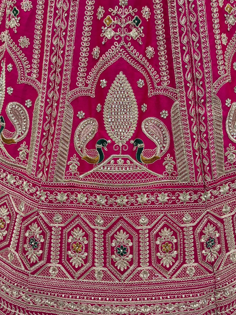 Close-up of pink ethnic lehenga fabric with gold embroidery and peacock motifs