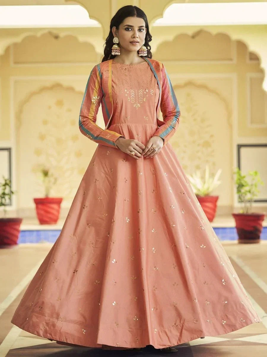 Woman wearing peach ethnic gown with gold embroidery and colorful long sleeves, indoor setting