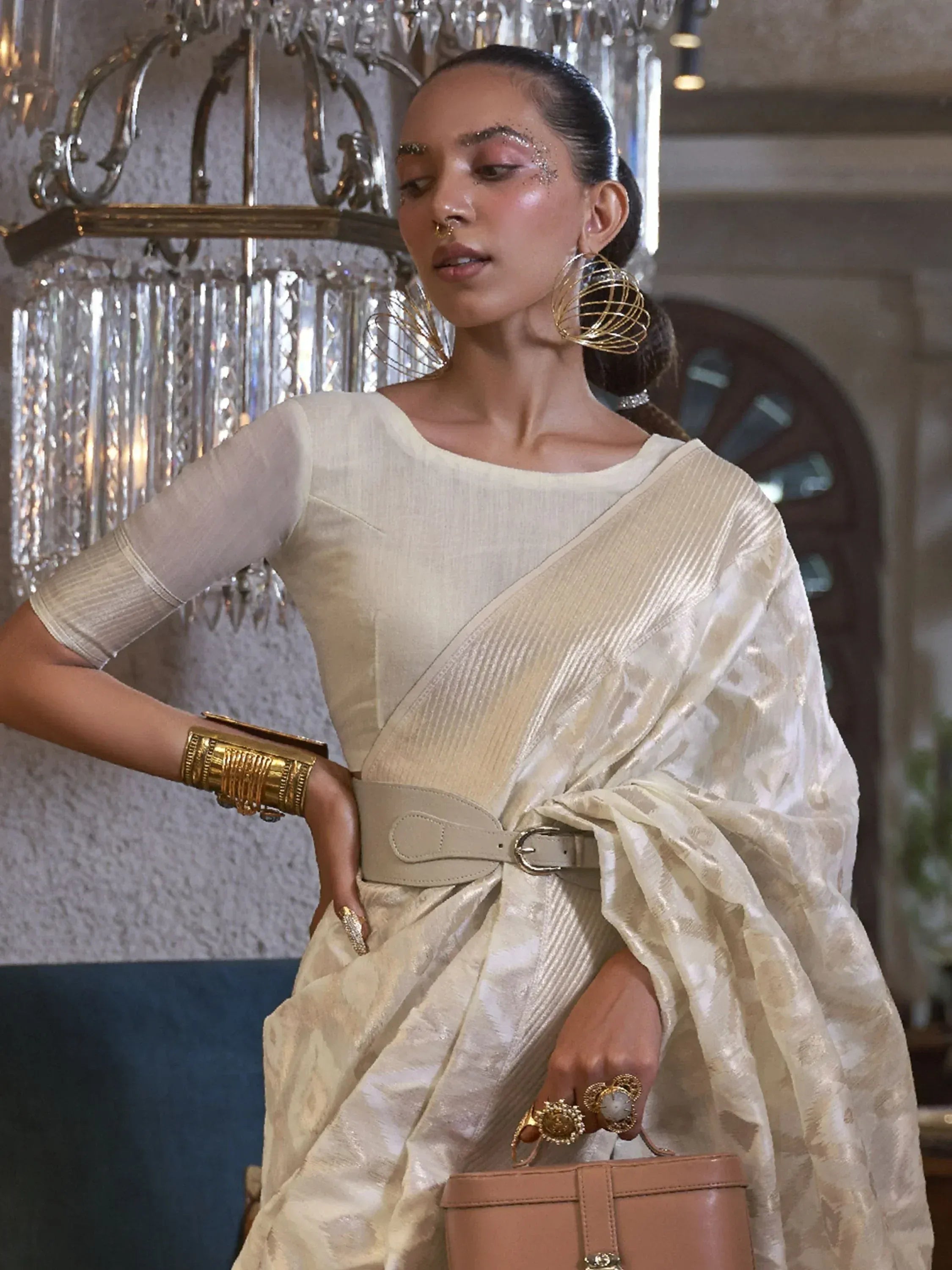 Elegant woman in cream designer saree with gold jewelry and belt, styled for ethnic occasions
