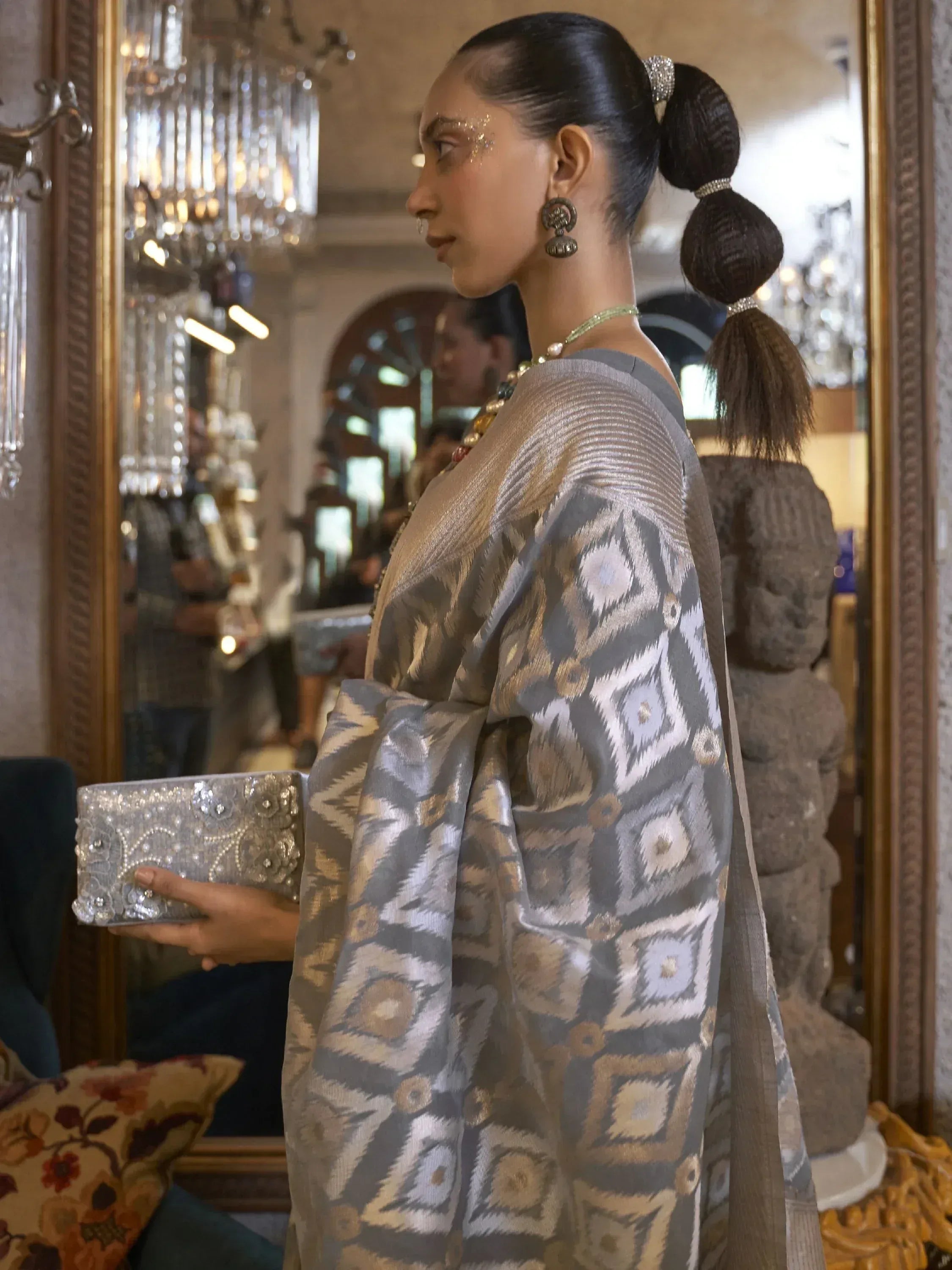Woman in elegant grey and gold ikat saree with traditional jewelry and embellished clutch, luxury ethnic wear