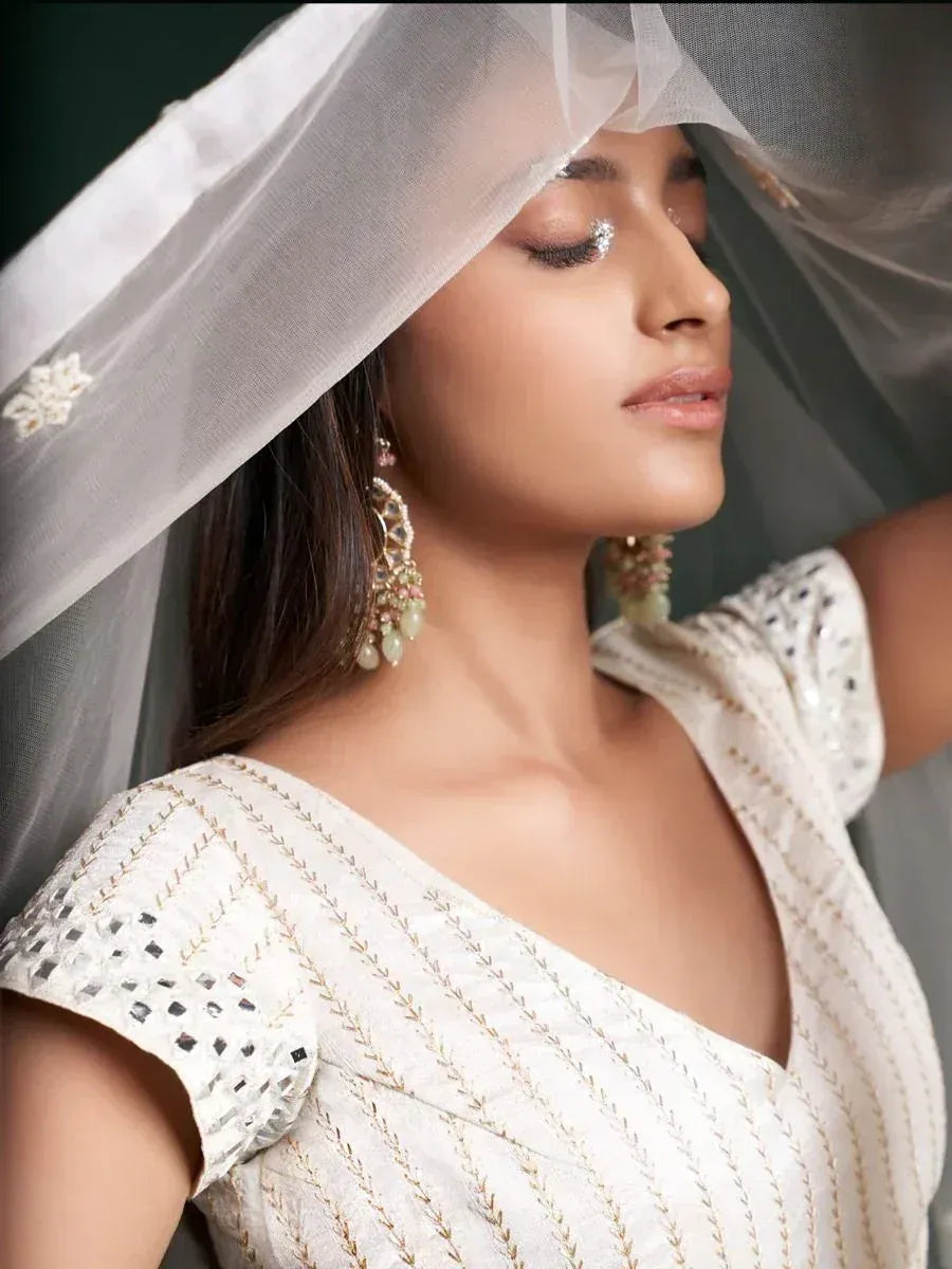 Elegant white ethnic gown with gold embroidery, sheer dupatta, and statement earrings for Indian weddings