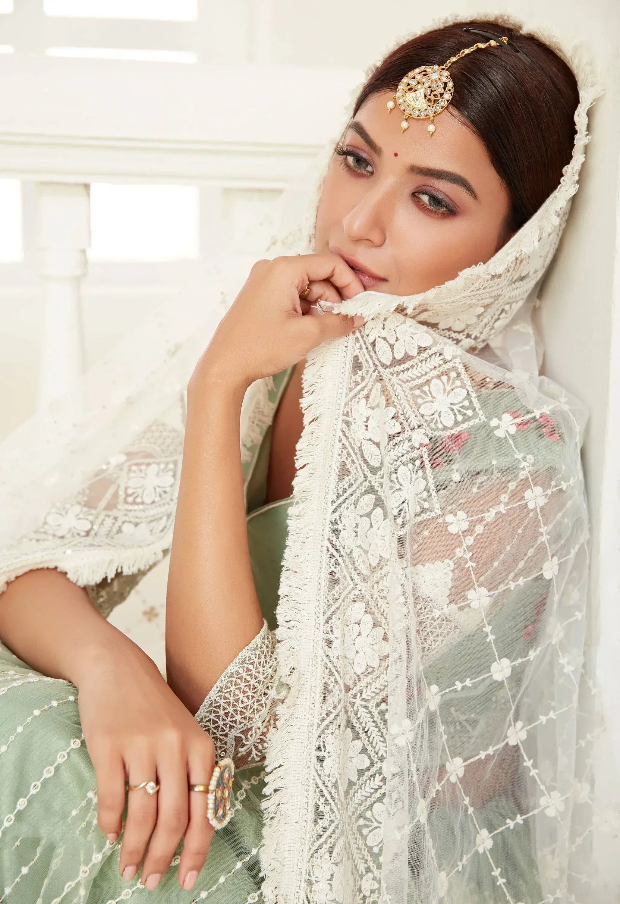 Elegant woman in mint green ethnic gown with white lace dupatta and gold maang tikka, perfect for Indian weddings.