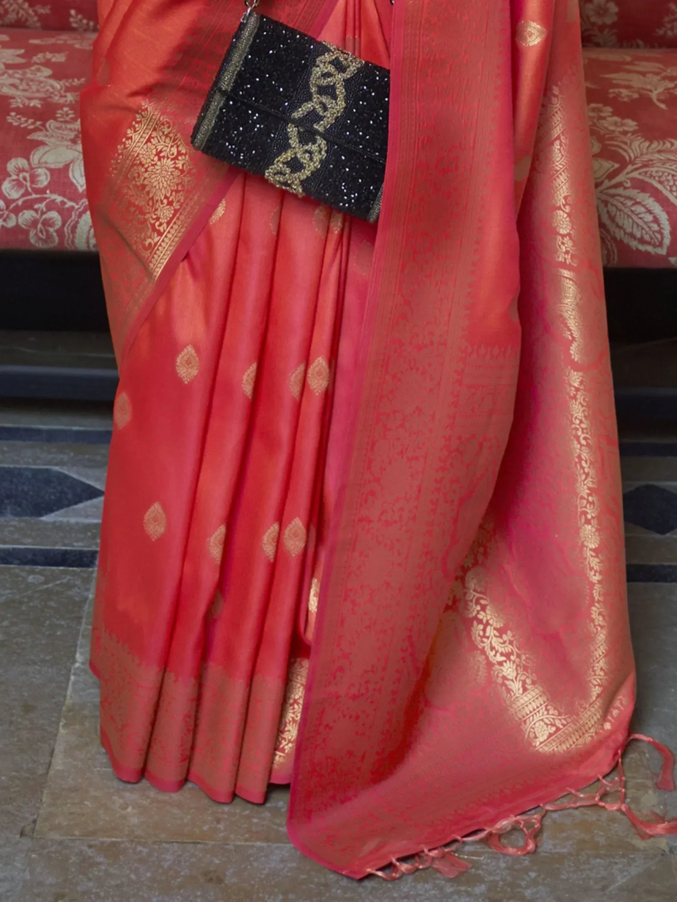 Red silk saree with gold zari work, paired with black beaded clutch, perfect for Indian ethnic occasions.