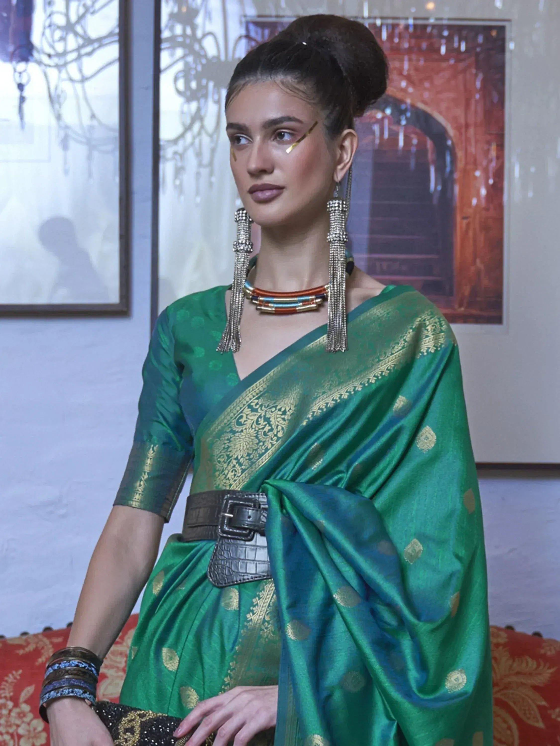 Emerald green designer saree with gold embroidery, paired with statement jewelry and a modern belt for ethnic wear.
