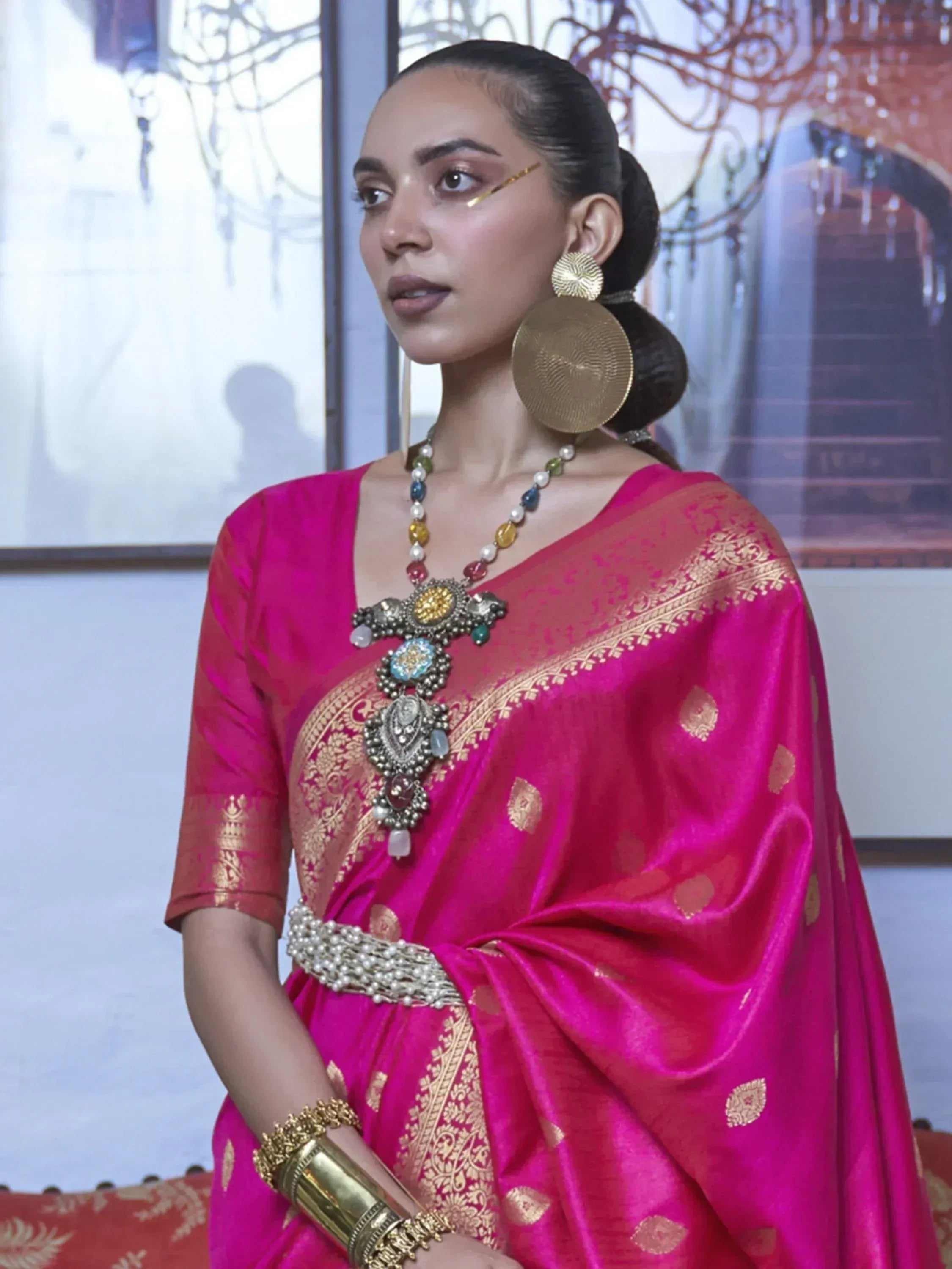 Woman in vibrant pink ethnic saree with gold embroidery, statement jewelry, and traditional Indian attire