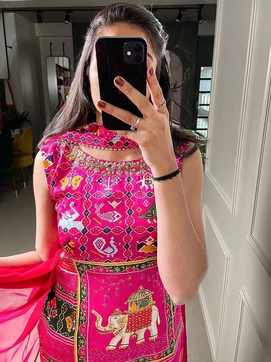 Woman in bright pink ethnic Indian printed saree with animal motifs, taking mirror selfie indoors