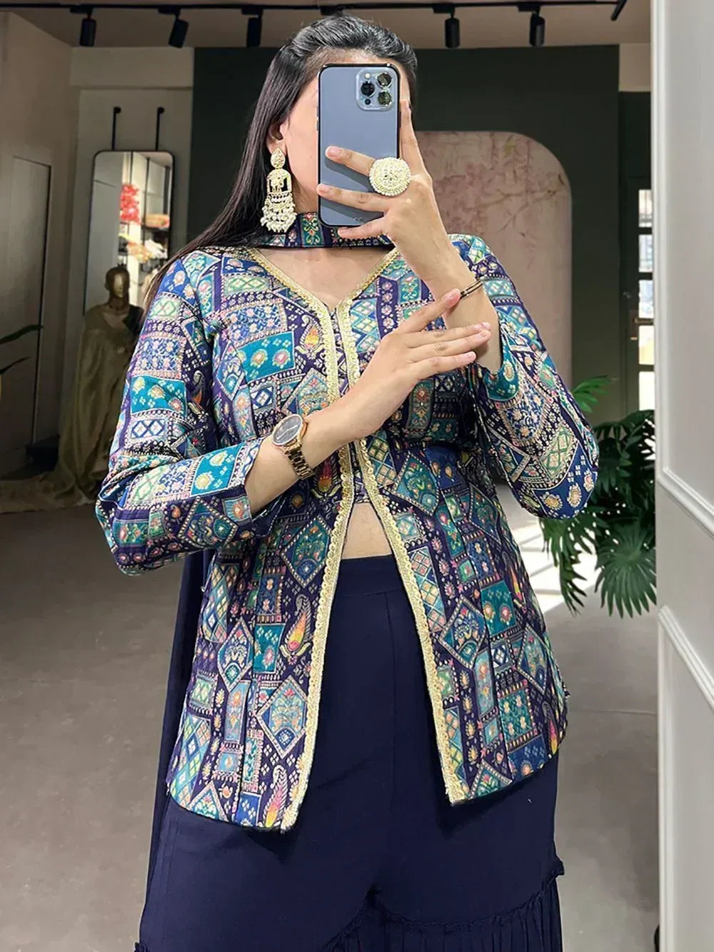 Woman wearing colorful printed ethnic jacket with gold trim, paired with navy palazzo pants, taking mirror selfie