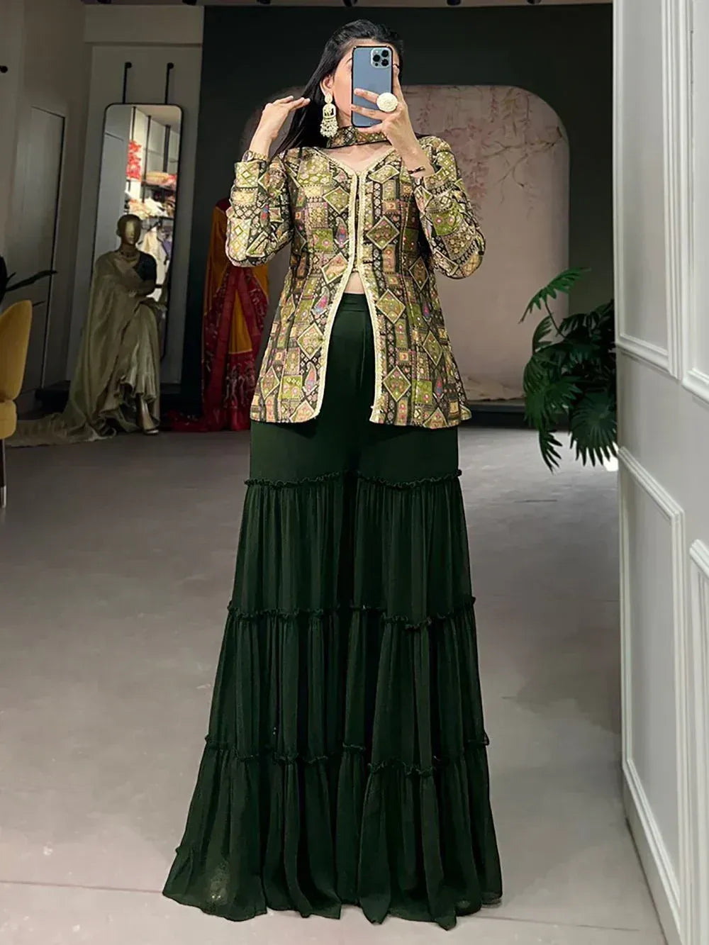 Woman in printed ethnic jacket with tiered green palazzo pants, mirror selfie in boutique