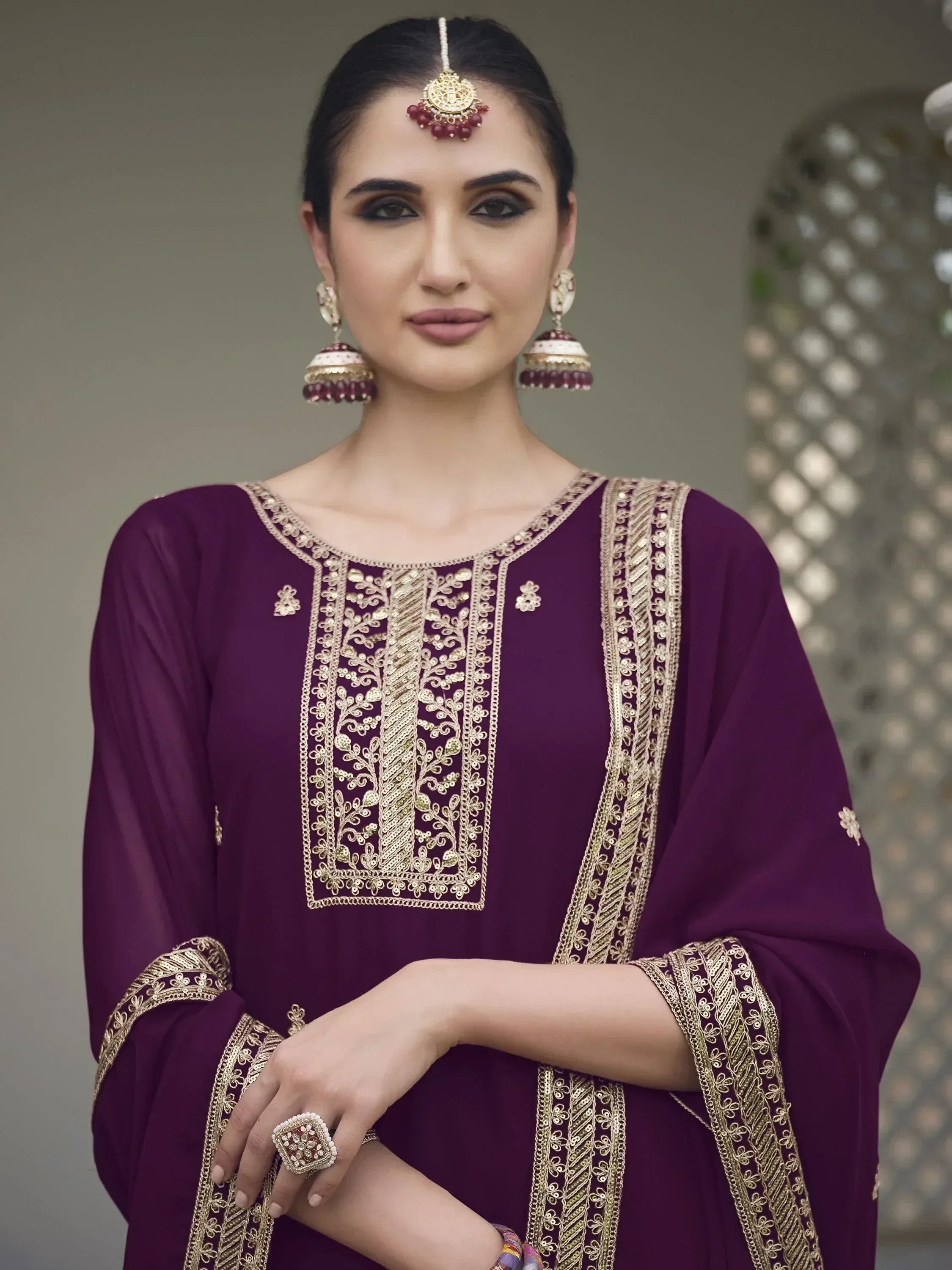 Woman in purple embroidered salwar kameez with gold jewelry and traditional makeup
