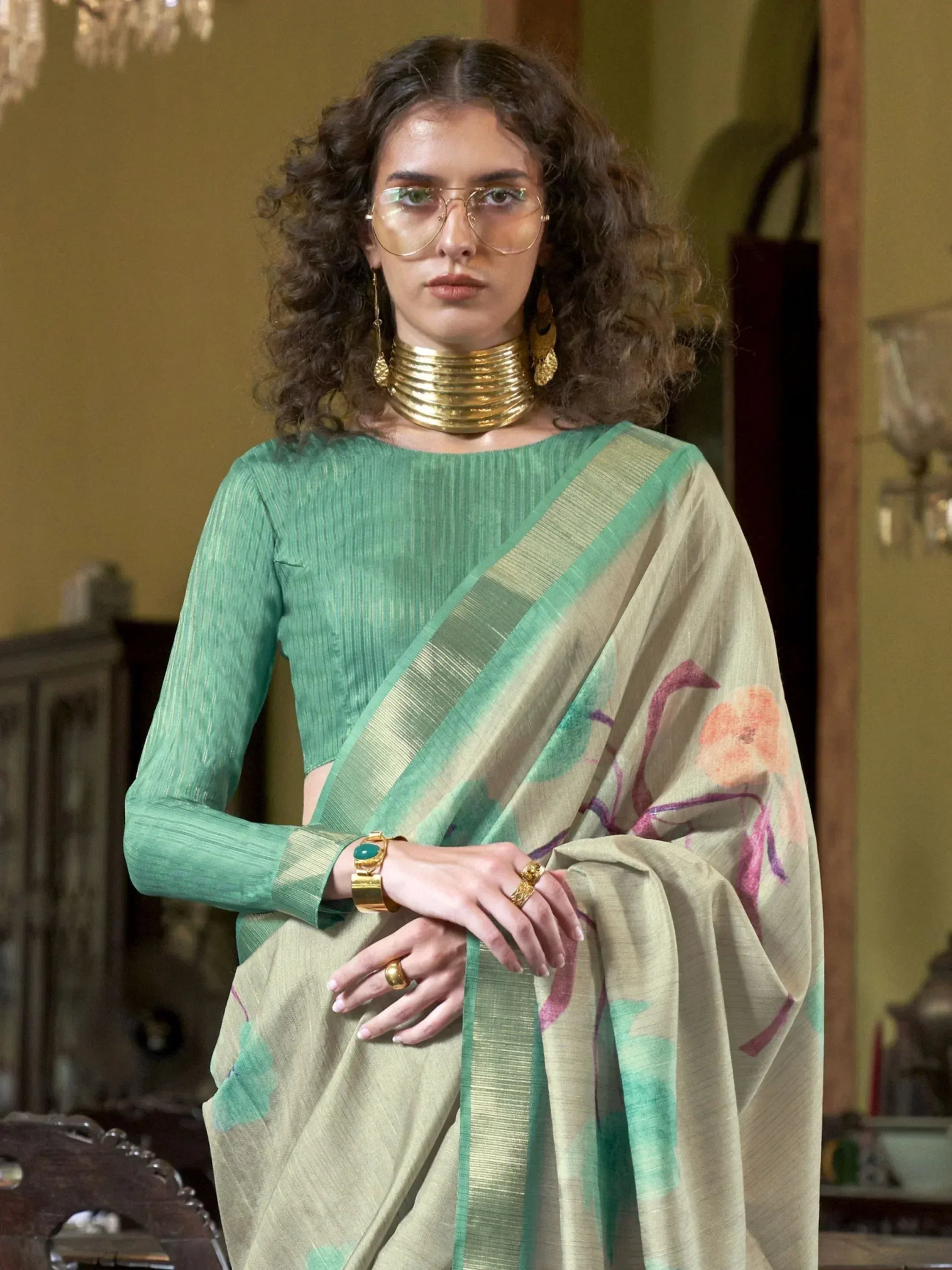Woman in green designer saree with floral print, gold jewelry, and statement glasses for ethnic wear