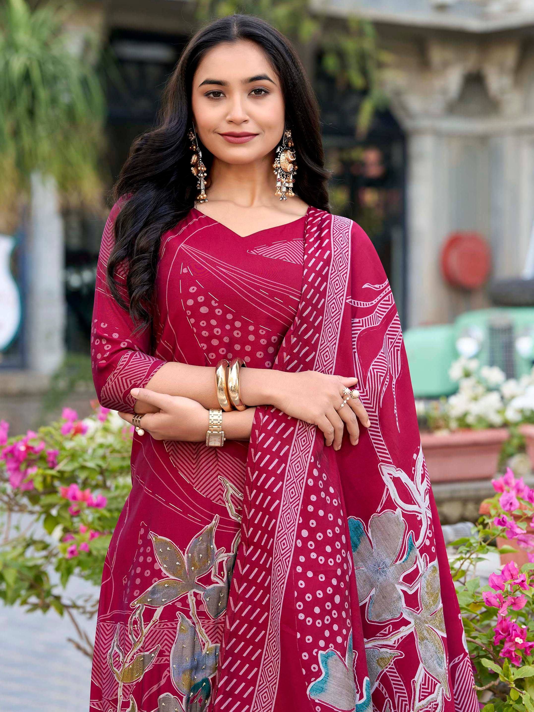 Woman in maroon printed ethnic gown with floral and geometric patterns, styled with gold jewelry for festive occasions